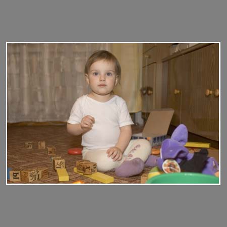 Полуторагодовалая девочка играет с игрушками, сидя на полу